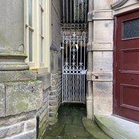 Small white gate, between two buildings and next to maroon door