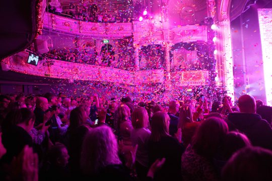 Audience standing and clapping with confetti in the air at the end of a show