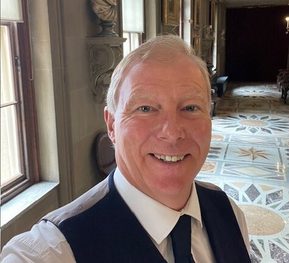 white man smiling in a white shirt, black waistcoat and black tie
