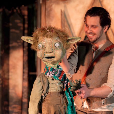 Male performer holding puppet Rumpelstiltskin with pointy ears ad wide eyes