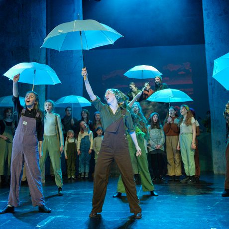 Group of performers holding blue umbrellas up in the air