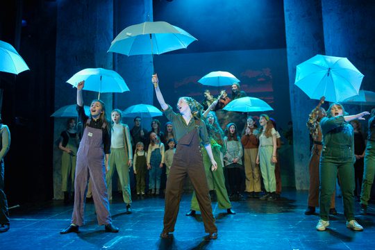 Group of performers holding blue umbrellas up in the air