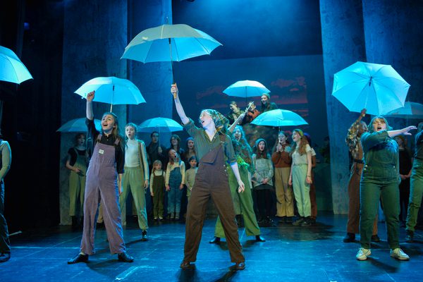 Group of performers holding blue umbrellas up in the air