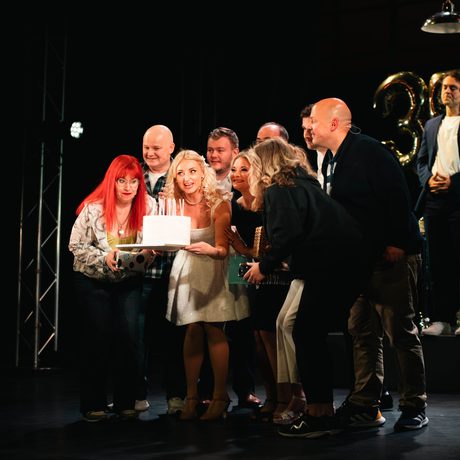 Group of performers on stage blowing out candles on cake