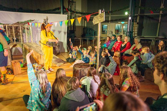 Performer dressed in yellow as rabbit performing to audience of children with their hands up