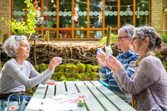 three people sat around picnic bench holding up their origami creations