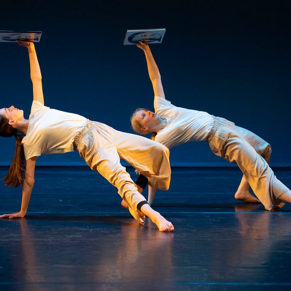 Two dancers, both with one arm on floor and one holding up image