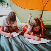 Two young people lay on the floor writing, under a tent