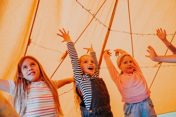 Three young children with their arms upstretched in a tent