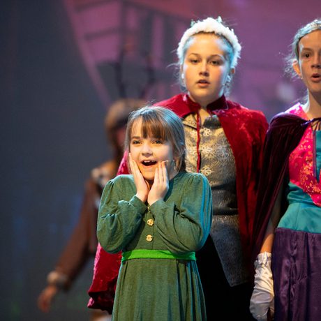 Young performer in green dress holding hands to both cheeks in look of delight