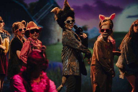 Young performers in animal costumes and sunglasses, central performer holding microphone and looking to audience