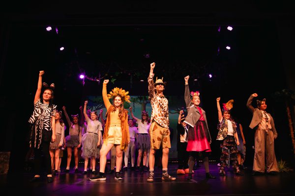 Group of young people on stage dressed as animals with hands in the air