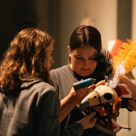 Two young people gluing feathers onto a decorative headdress