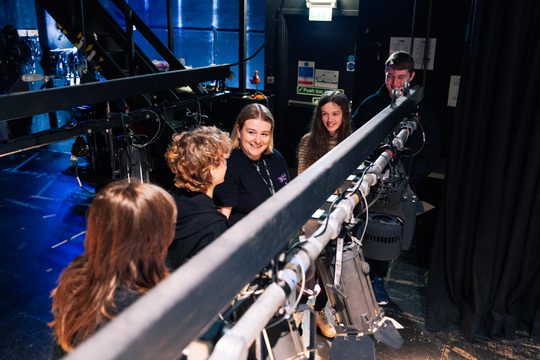 An image of four technical youth theatre participants learning from our resident Technician. They are studying a lighting rig.