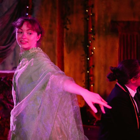 Female performer in green dress turning to look back, with arm pointed out to side