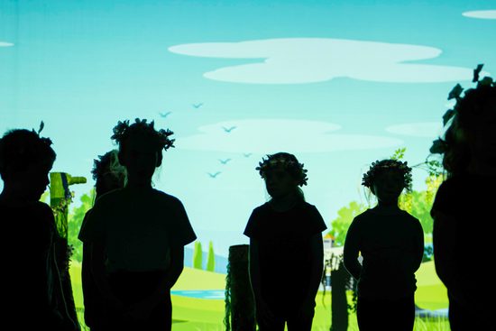 Silhouette of young performers wearing flower crowns against a projected green landscape behind them