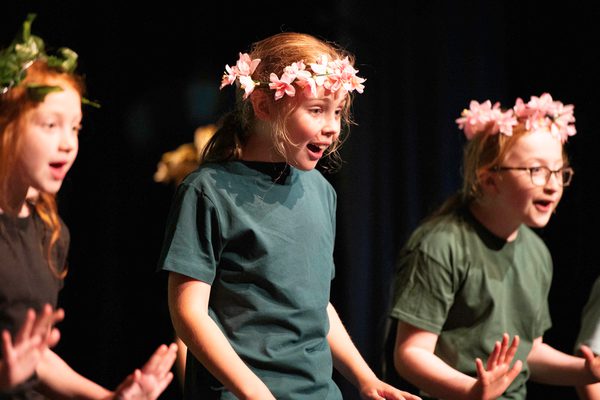 Three young performers singing to audience, they all wear flower crowns.