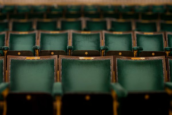 Empty theatre seats focused on gold name plate above the green back cushion.