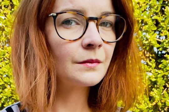 A woman with shoulder length, auburn hair is wearing glasses and looking directly at the camera against a backdrop of greenery, a book titled 'Radio Universe' by Emma Chapman sits in the top right-hand corner.