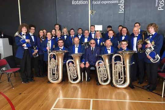 A brass band wearing blue jackets and holding their instruments.