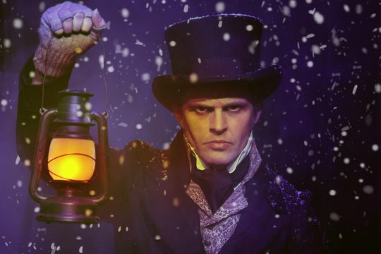 A man in a top hat, holding a lamp and standing in the snow.