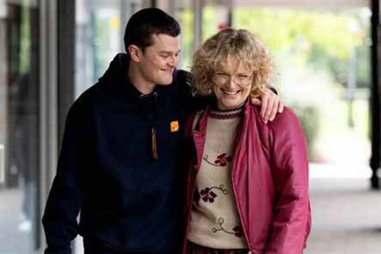 A young man in a black hoodie embracing an older woman in a pink coat.