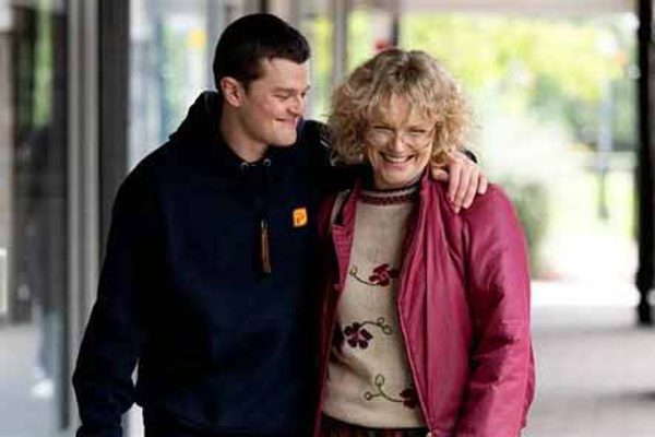 A young man in a black hoodie embracing an older woman in a pink coat.