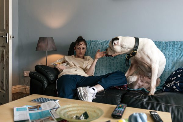 A woman looking tired, sitting on a sofa and petting a dog.