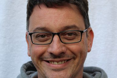 A man with brown hair wearing glasses and a grey hoodie.