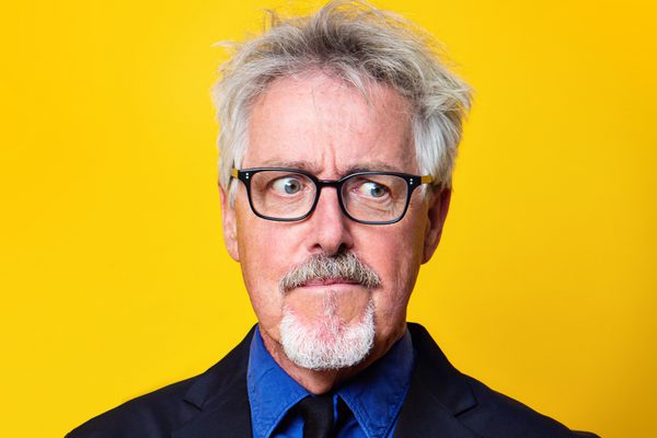Griff in a suit and tie with blue shirt and black glasses.