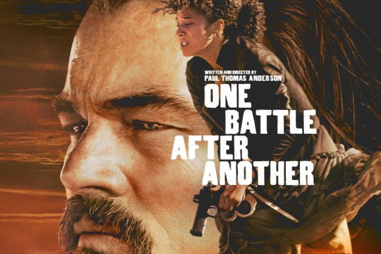 Close up of a man's face in front of a sunset. A woman is running and holding a gun.