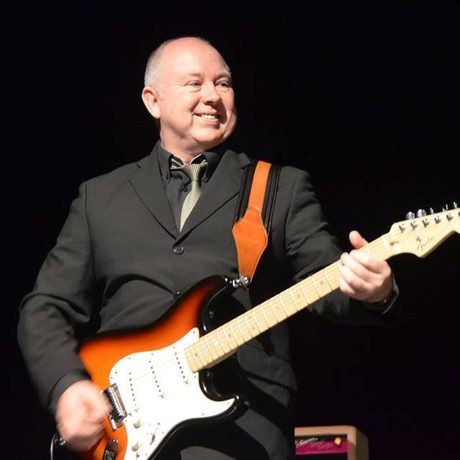 Guitarist dressed in all black playing an orange electric guitar