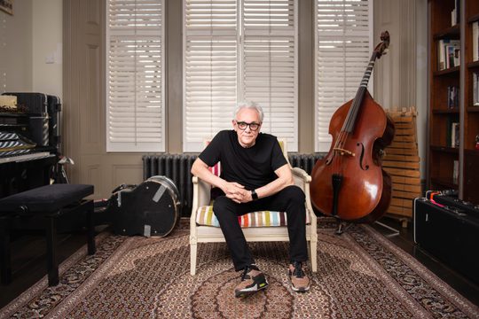 Trevor, dressed in all black sat on chair surrounded by different musical instruments