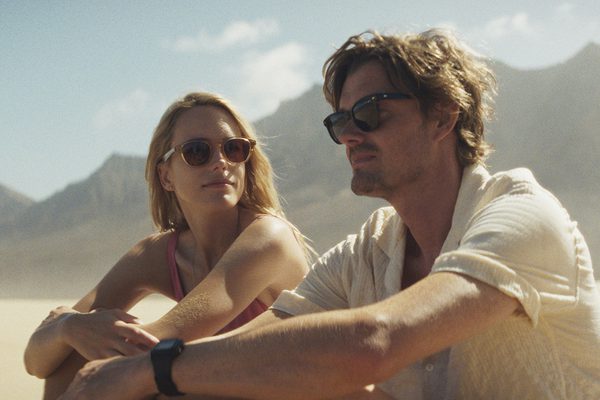 A man and a woman wearing sunglasses sat on a beach.