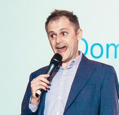 A man in a blue jacket with short brown hair speaking into a microphone.