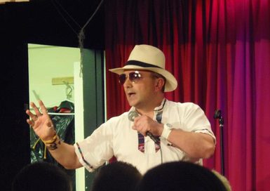 A man sat down, wearing a wide-brimmed hat and sunglasses, holding a microphone.