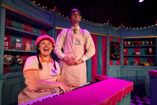 A man and a woman in an ice cream shop singing at a pink piano.