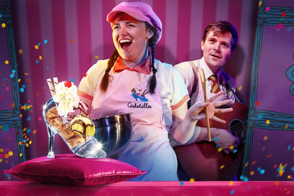 A man and a woman in aprons standing behind a glass slipper full of ice cream.