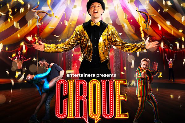A man standing in a gold jacket and bow tie in the middle of a circus.