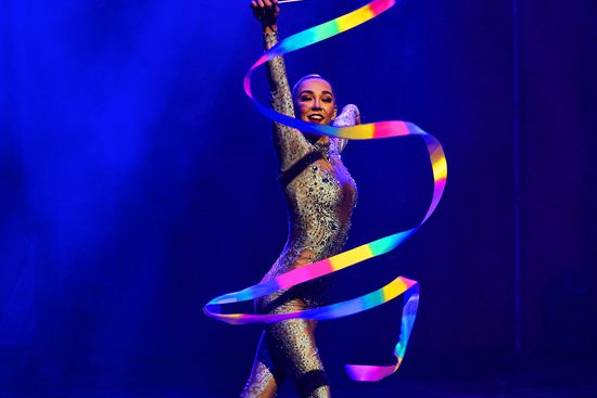 A girl in a leotard dancing with a rainbow coloured ribbon.