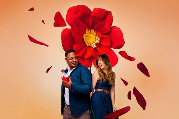 A man and a woman standing underneath a big red flower.