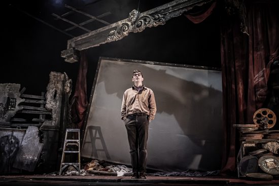 A man in brown clothes standing in an abandoned cinema.