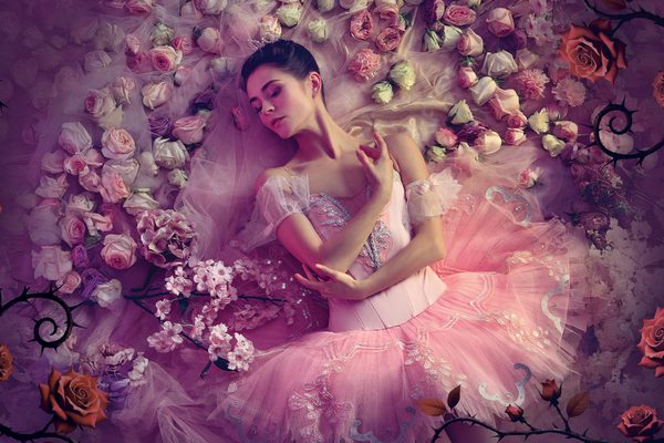 A ballerina lying down surrounded by pink flowers.
