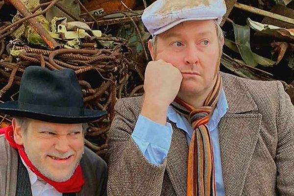 Two men in flat caps, scarves, and slightly worn-down clothes.