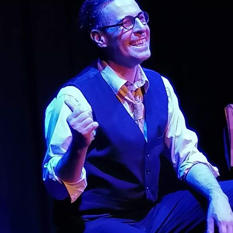 A man sat down, pointing behind himself and smiling.