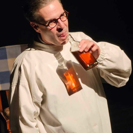 A man wearing a white shirt drinking from a glass bottle.