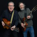 Tom Robinson and Adam Phillips standing with guitars and smiling.