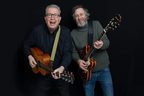 Tom Robinson and Adam Phillips standing with guitars and smiling.