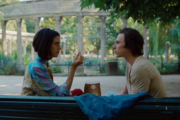 A man and a woman sat on a green bench looking at each other.