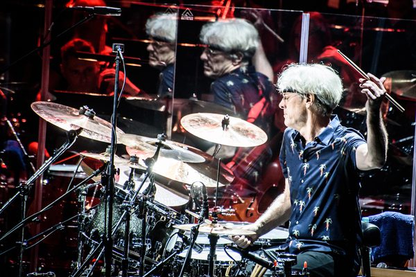 Stewart sat playing the drums wearing a blue shirt covered in palm trees.